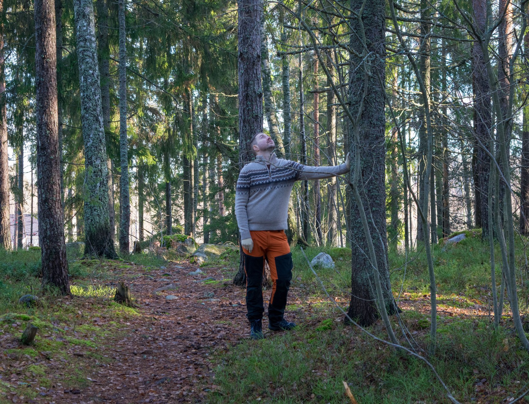 Lauri Lavanti retkeilyvaatteissa metsässä, nojaa puuhun ja katsoo ylös sen runkoa.