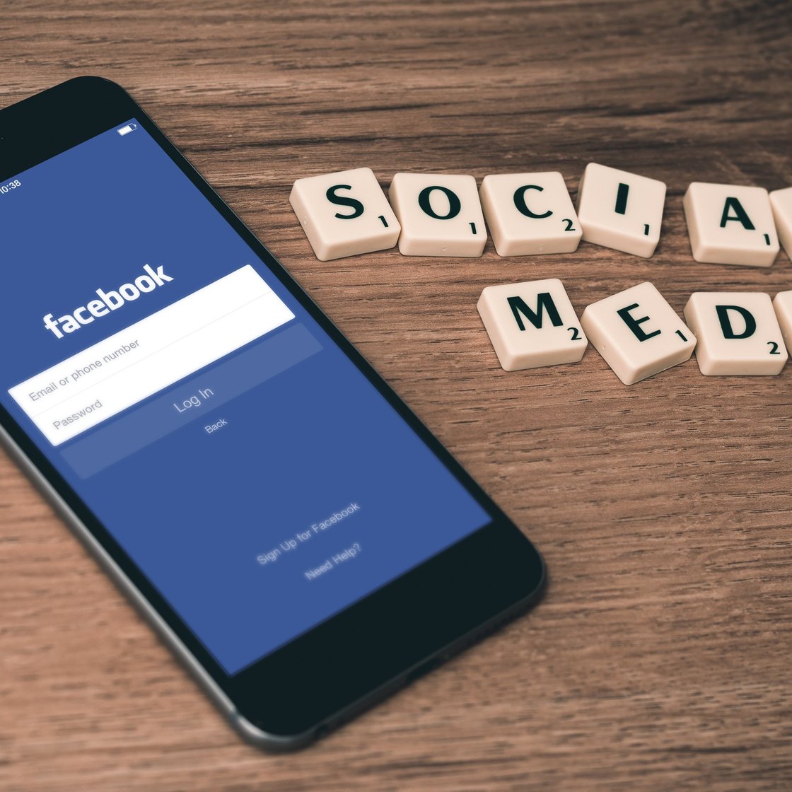 Puhelin, jossa on auki Facebookin sovellus odottamassa kirjautumistietoja sekä Scrabble-pelistä tutuilla nappuloilla tehty teksti "Social media"
