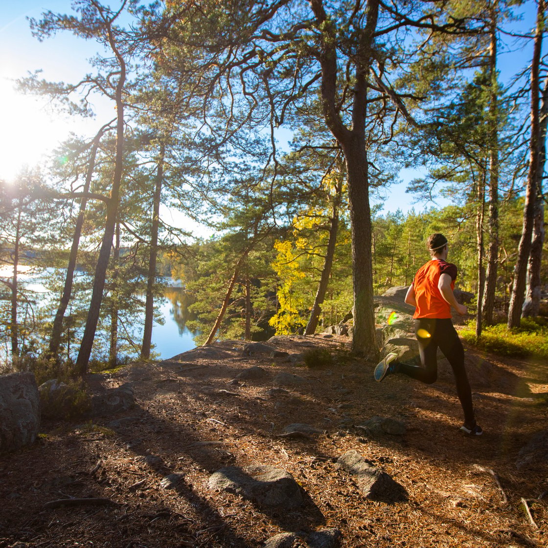 Kuvassa on ihminen juoksemassa metsässä. Taustalla näkyy järvi ja kirkkaana loistava aurinko.