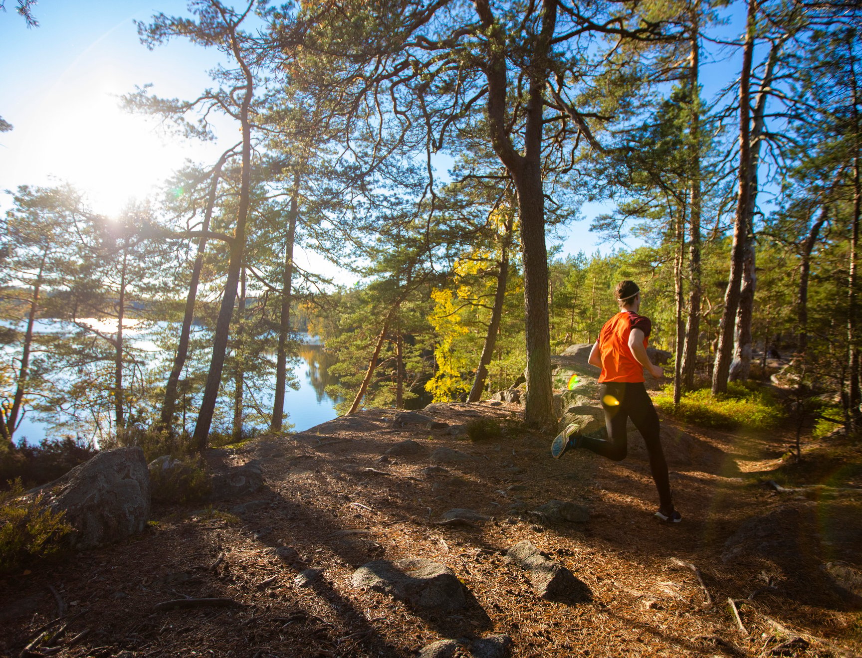 Kuvassa on ihminen juoksemassa metsässä. Taustalla näkyy järvi ja kirkkaana loistava aurinko.