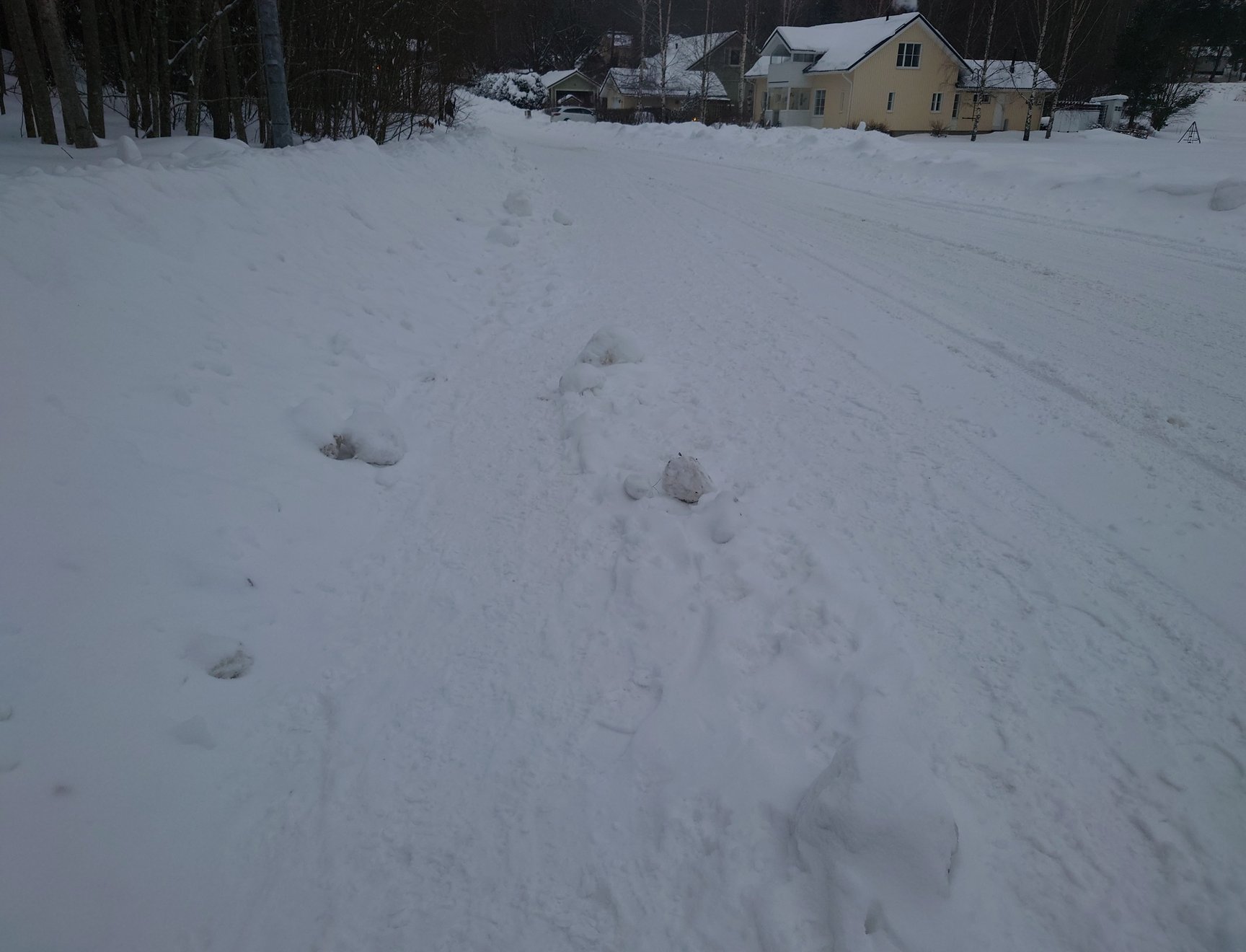 Kuva huonosti auratusta jalkakäytävästä, jonka vieressä on huolella aurattu autotie.
